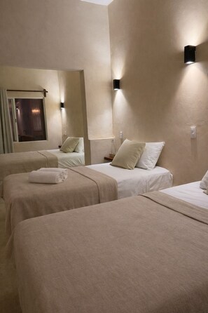 Habitación de hotel con tres camas, cada una con una manta y almohadas color beige, y una ventana con cortinas.