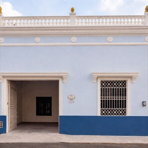 Un edificio con fachada azul claro, un balcón blanco con barandilla y una puerta negra.