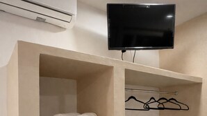 A hotel room with a flat-screen TV mounted on the wall, a shelf with rolled towels, a basket, and a clothing rack. - Chulel Hotel Origen (Mérida)