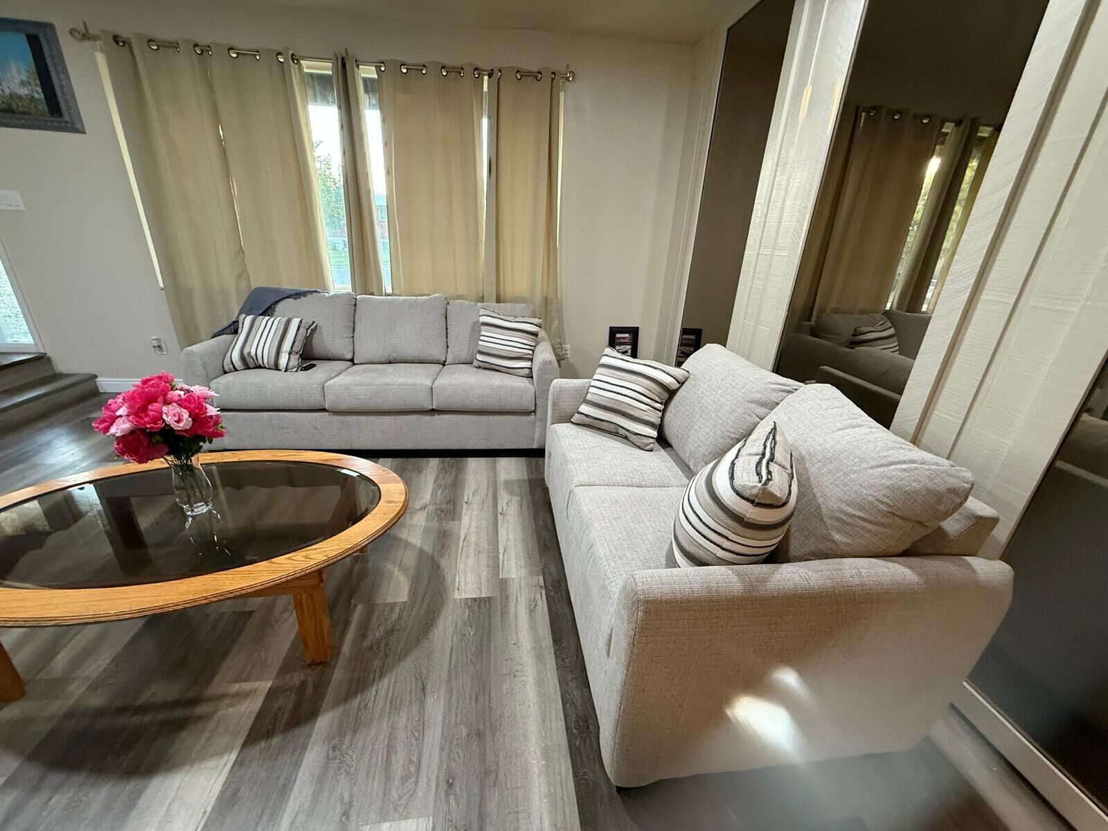 A modern living room with a grey sofa, a beige sofa, a glass coffee table, and a vase of pink flowers.