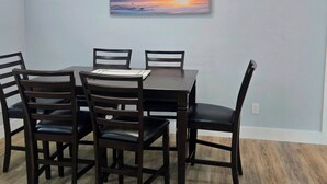 Un coin repas avec une table et des chaises, un luminaire au plafond et un tableau représentant un coucher de soleil accroché au mur.