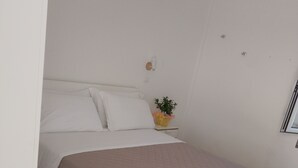 Een slaapkamer met een bed, een nachtkastje met een plantje en een wandlamp.