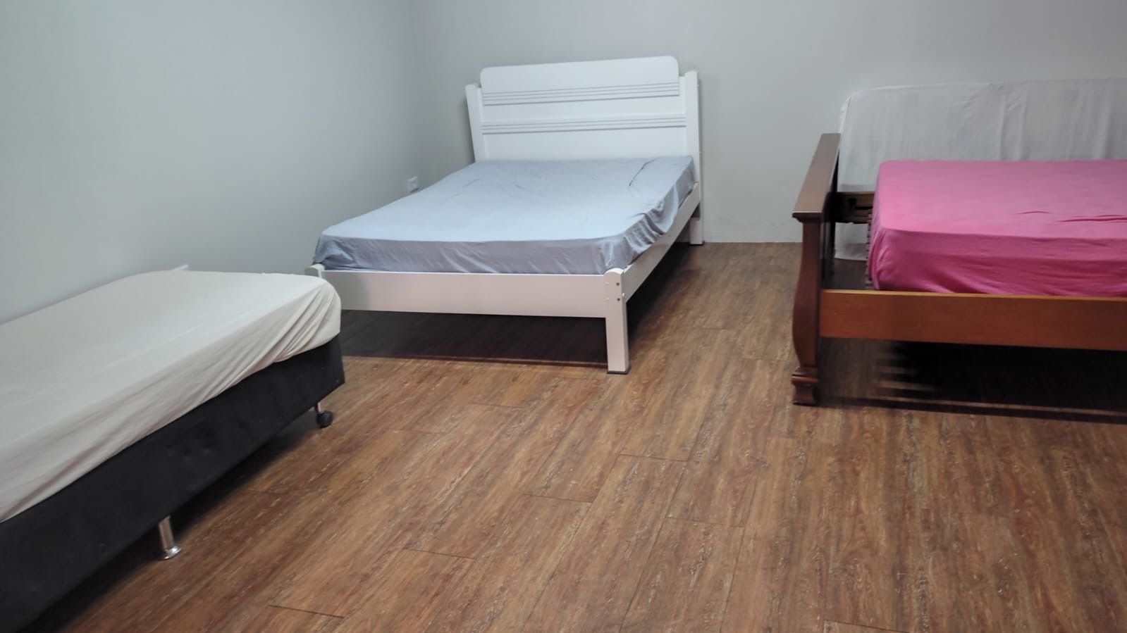 A room with three beds, each with different bedding, and a wooden floor.