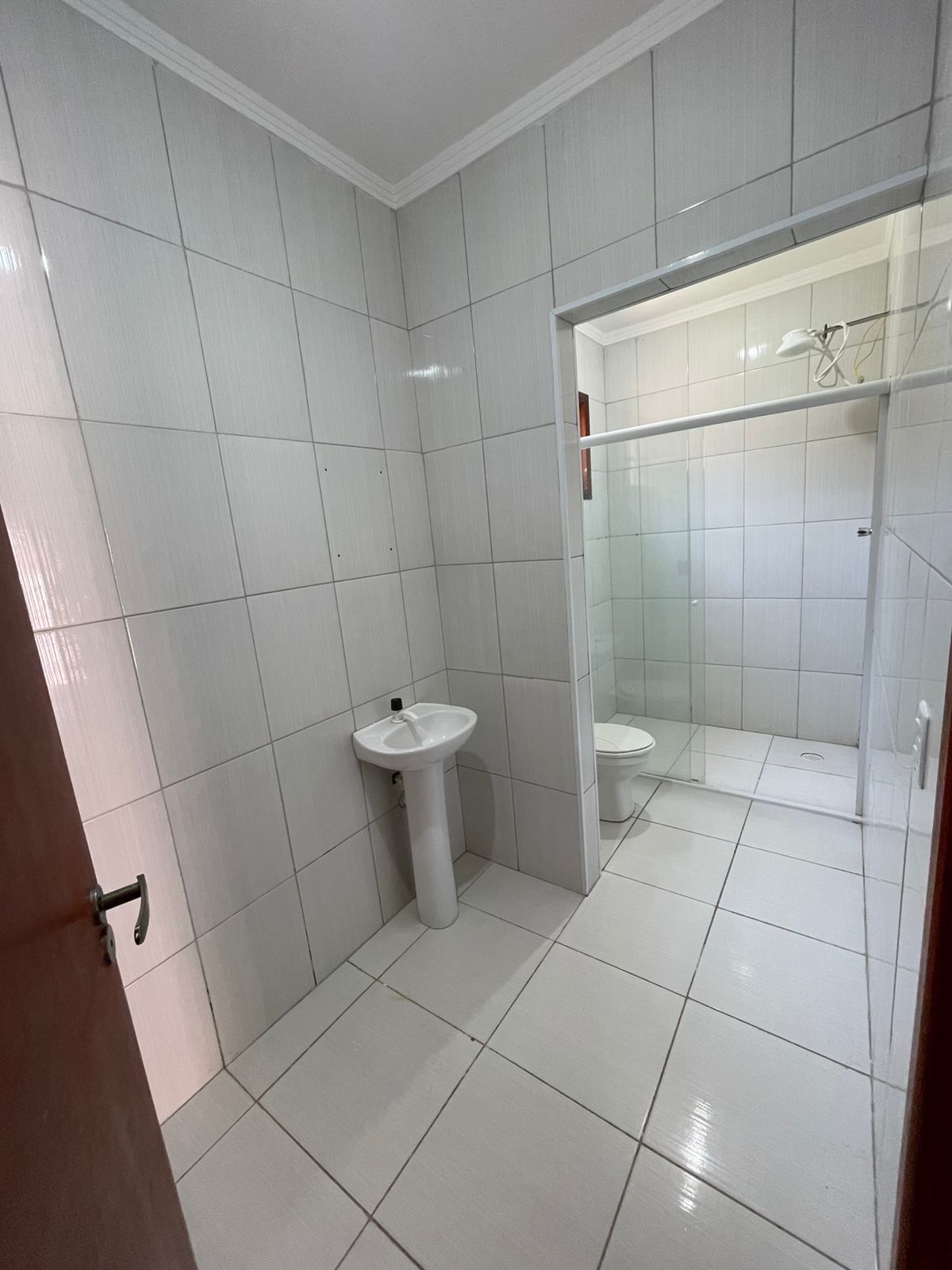 Un baño con azulejos blancos, un lavamanos y una zona de ducha con mampara de vidrio.