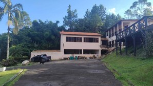 A two-story building with a flat roof and large windows, surrounded by lush greenery and a paved driveway. - FARM WITH 7 CHALETS PERFECT FOR THAT FAMILY MOMENT (Santa Isabel)