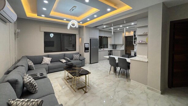 A modern living room with a grey sofa, a coffee table, and a dining area with chairs. - 3-bedroom apartment in lovely Amman with AC (Amman)