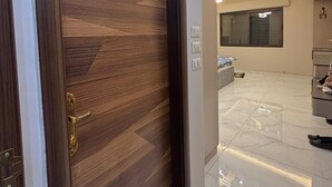A modern interior with a wooden door, a well-lit hallway, and a glimpse of a bedroom with a bed and a nightstand. - 3-bedroom apartment in lovely Amman with AC (Amman)
