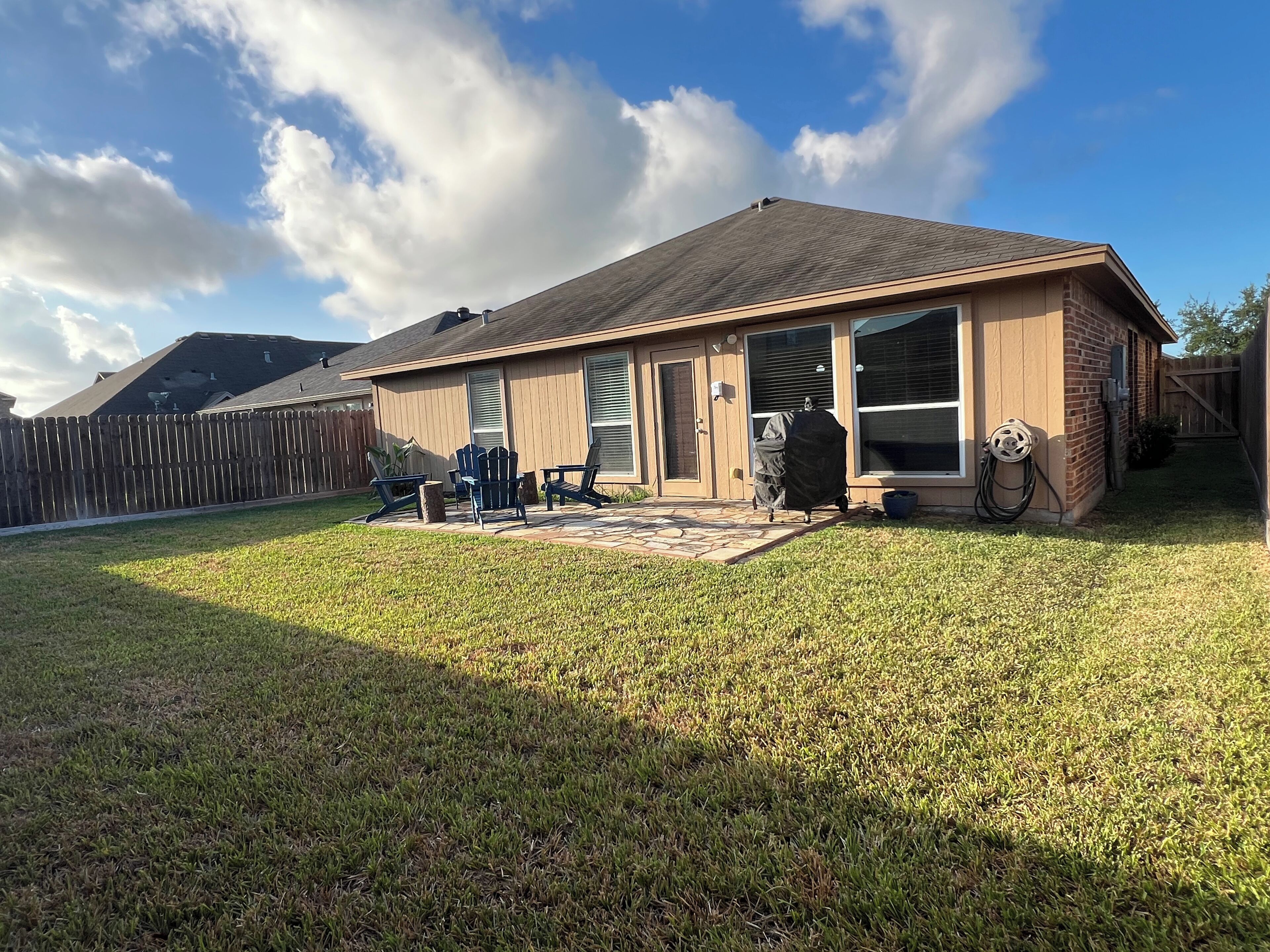 A house with a covered patio, a fenced yard, and a clear sky.