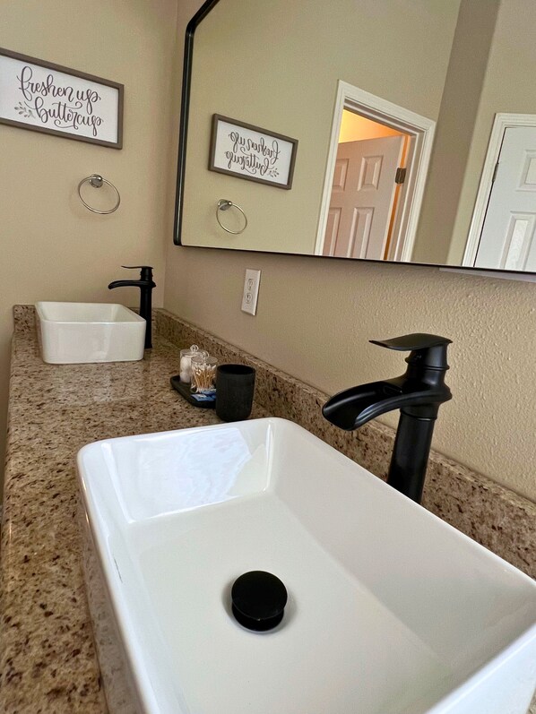 Une salle de bain avec un lavabo blanc, un robinet noir et deux panneaux encadrés accrochés au mur.