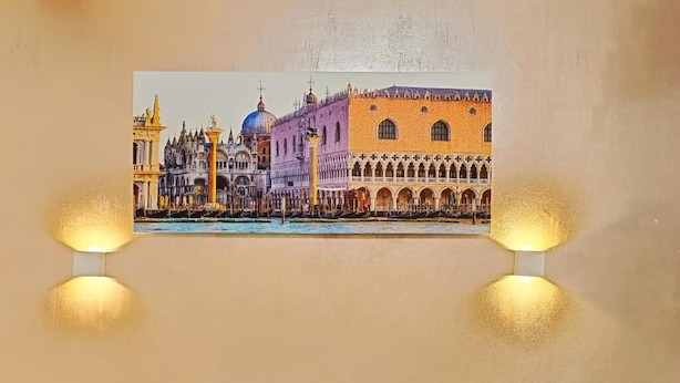 A framed picture of a historic building with arches and domes, displayed on a wall with two wall-mounted lights. - B&B Cavallotti (Mestre)