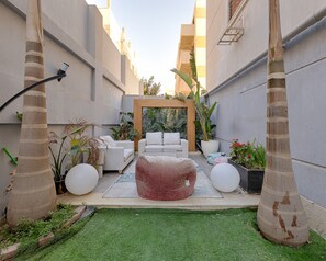 A modern outdoor seating area with a white sofa, a red bean bag, and a wooden archway. - ALSAWAH Spacious Garden Apartment in 9th District Sheikh Zayed (Sheikh Zayed City)