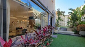 A modern house with a glass facade, a well-maintained garden, and a visible interior with a sofa and decorative items. - ALSAWAH Spacious Garden Apartment in 9th District Sheikh Zayed (Sheikh Zayed City)