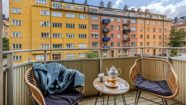 A balcony with wicker chairs, a small table with a teapot and croissants, and a view of multi-story buildings. - The Best Apartment in Stylish Sodermalm Stockholm (Stockholm)