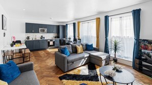A modern apartment with a grey sofa, a dining table, a kitchen, and a TV. - Stylish 2 Bed Apartment Central Brighton, The Lanes Sleeps 8 (Brighton and Hove)