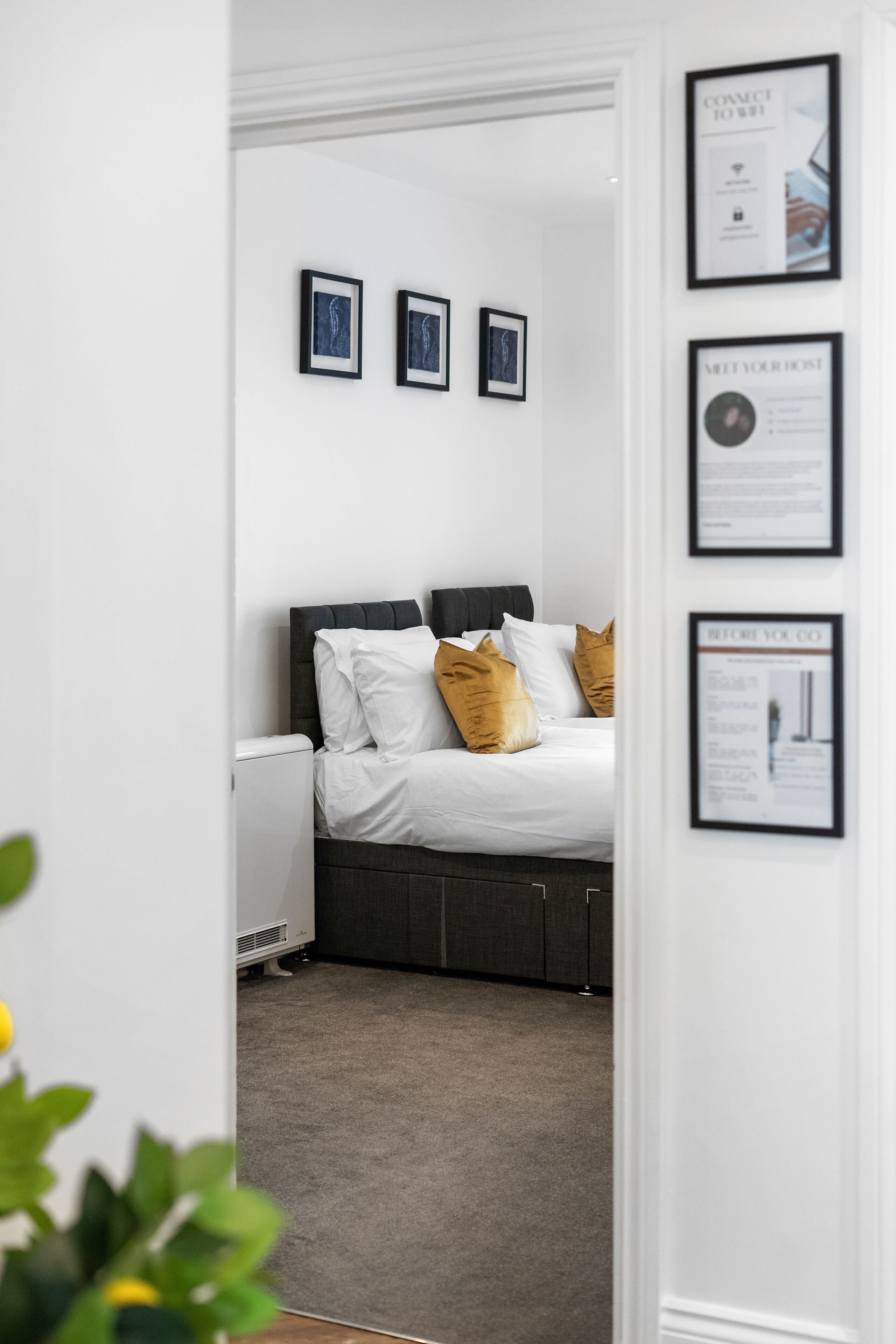 Een slaapkamer met een bed, witte muren en foto’s in lijsten aan de wand.