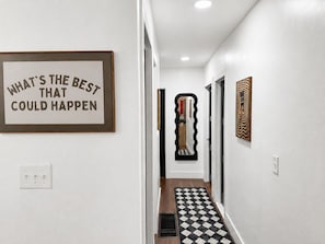 Un pasillo con una cita inspiradora enmarcada, un espejo decorativo y un tapete estampado.