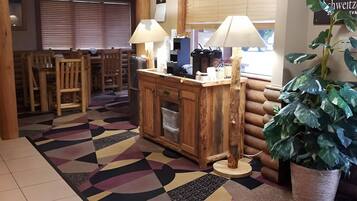 A cozy lobby with a wooden reception desk, two lamps, a large potted plant, and a patterned rug.