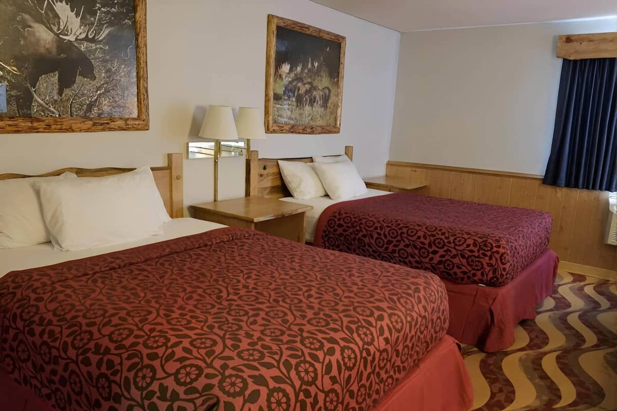A hotel room with two beds, a nightstand, a lamp, and two paintings on the wall.