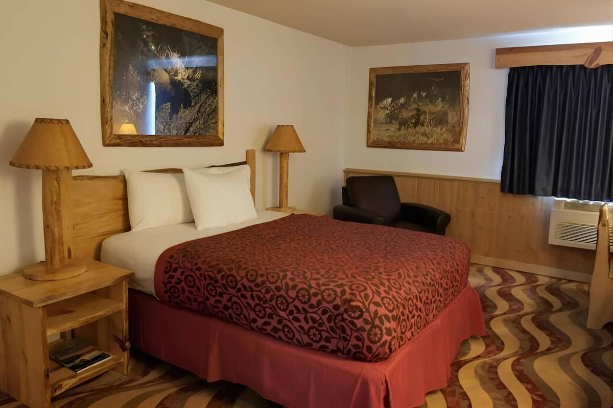 A hotel room with a large bed, two bedside tables with lamps, a chair, two framed pictures on the wall, and a patterned carpet.