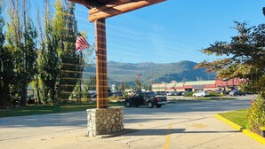 A covered parking area with a stone pillar, an American flag, and a view of a parking lot and mountains in the background.
