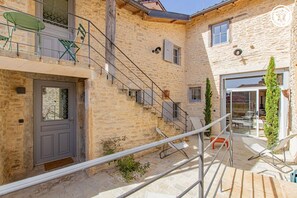 A stone building with a gray door, a staircase, and outdoor seating.