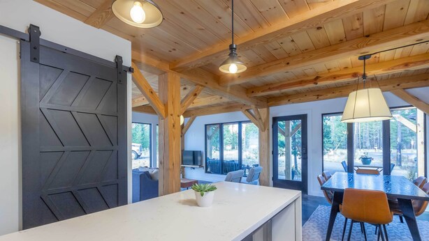 Une cuisine moderne avec un plan de travail blanc, une porte coulissante noire et un coin repas comprenant une table et des chaises.