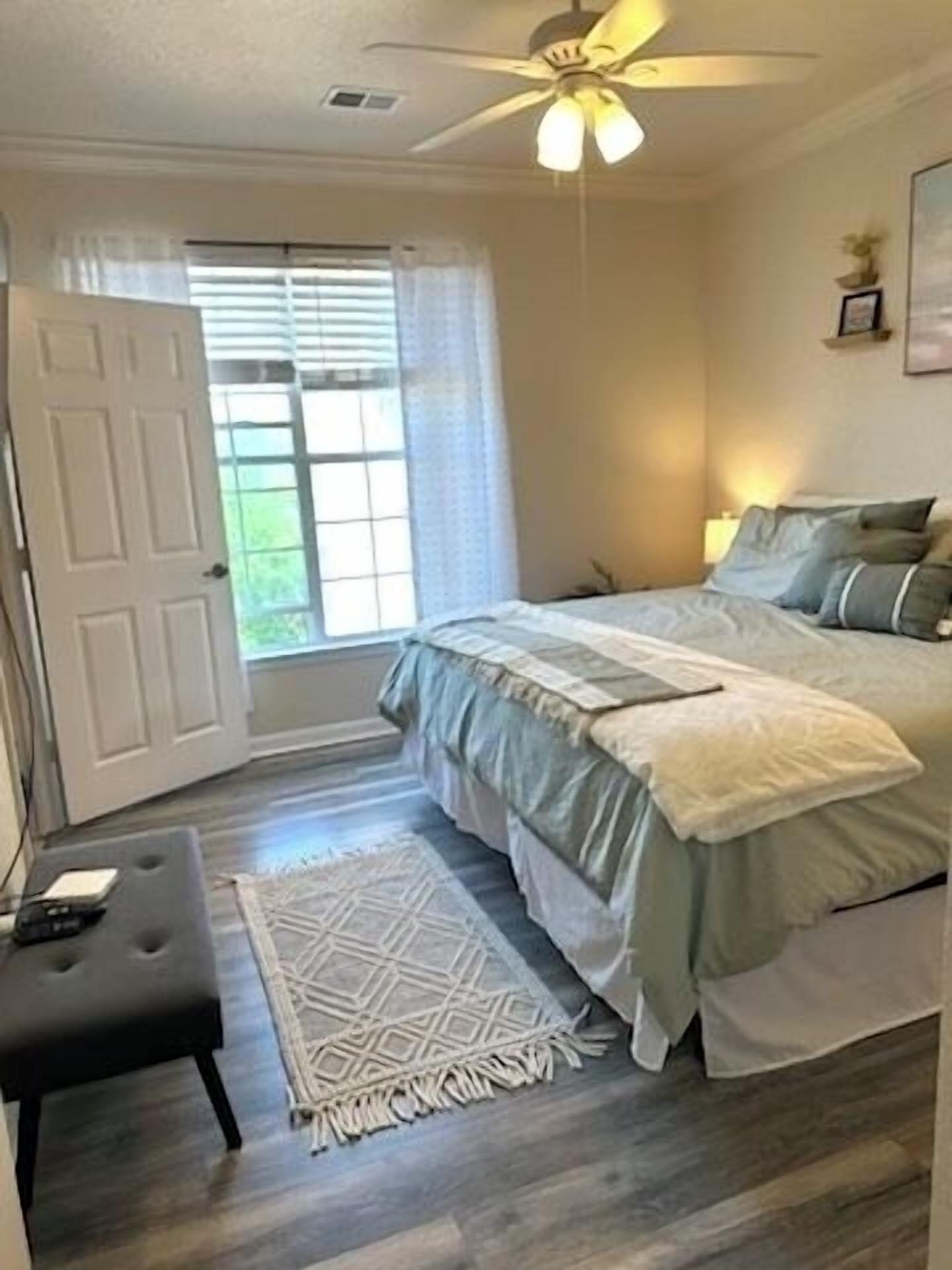 Ein Schlafzimmer mit einem Bett, Deckenventilator, einer Tür und einem Fenster mit Jalousien.