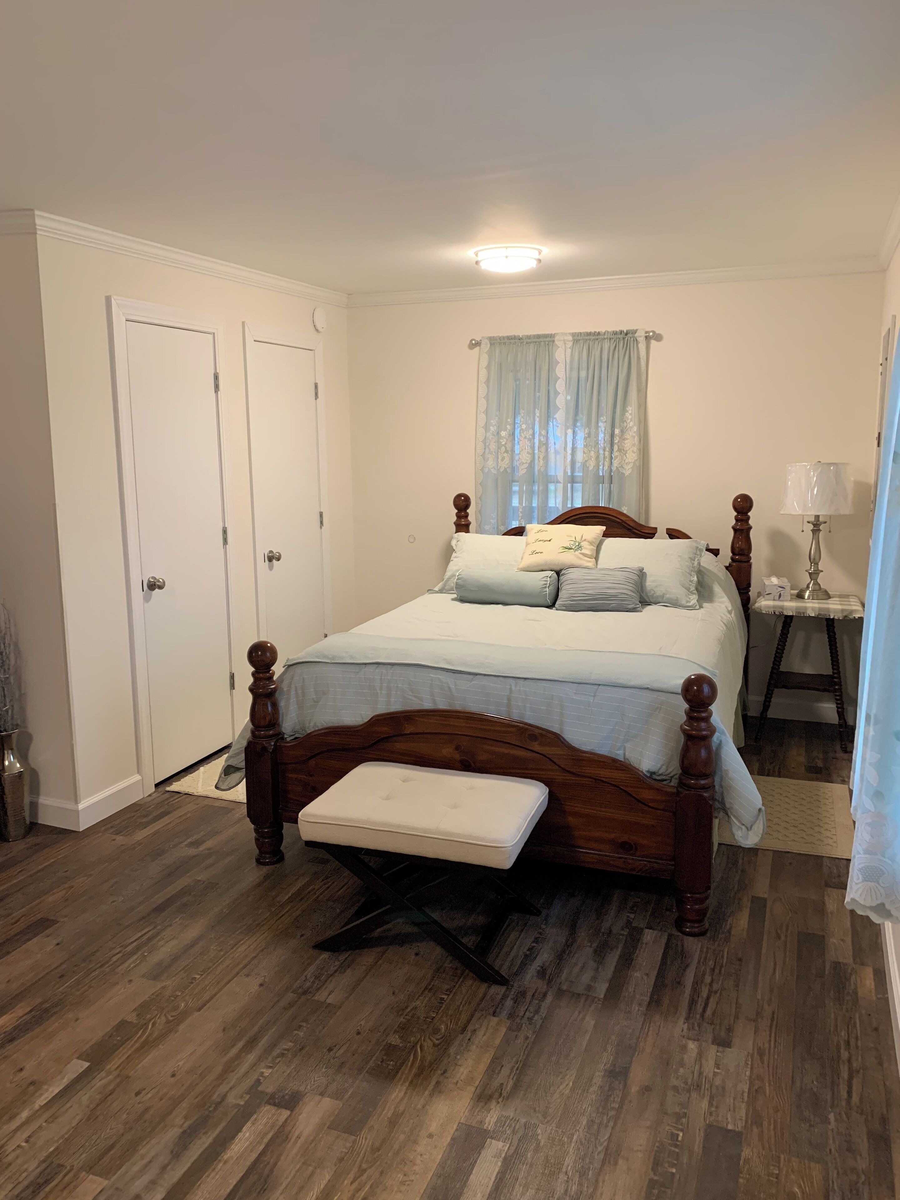 Une chambre à coucher avec un lit en bois, une table de chevet avec une lampe, un banc et une fenêtre avec des rideaux.