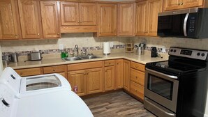 Una cocina con armarios de madera, microondas de acero inoxidable, horno doble y lavadora.