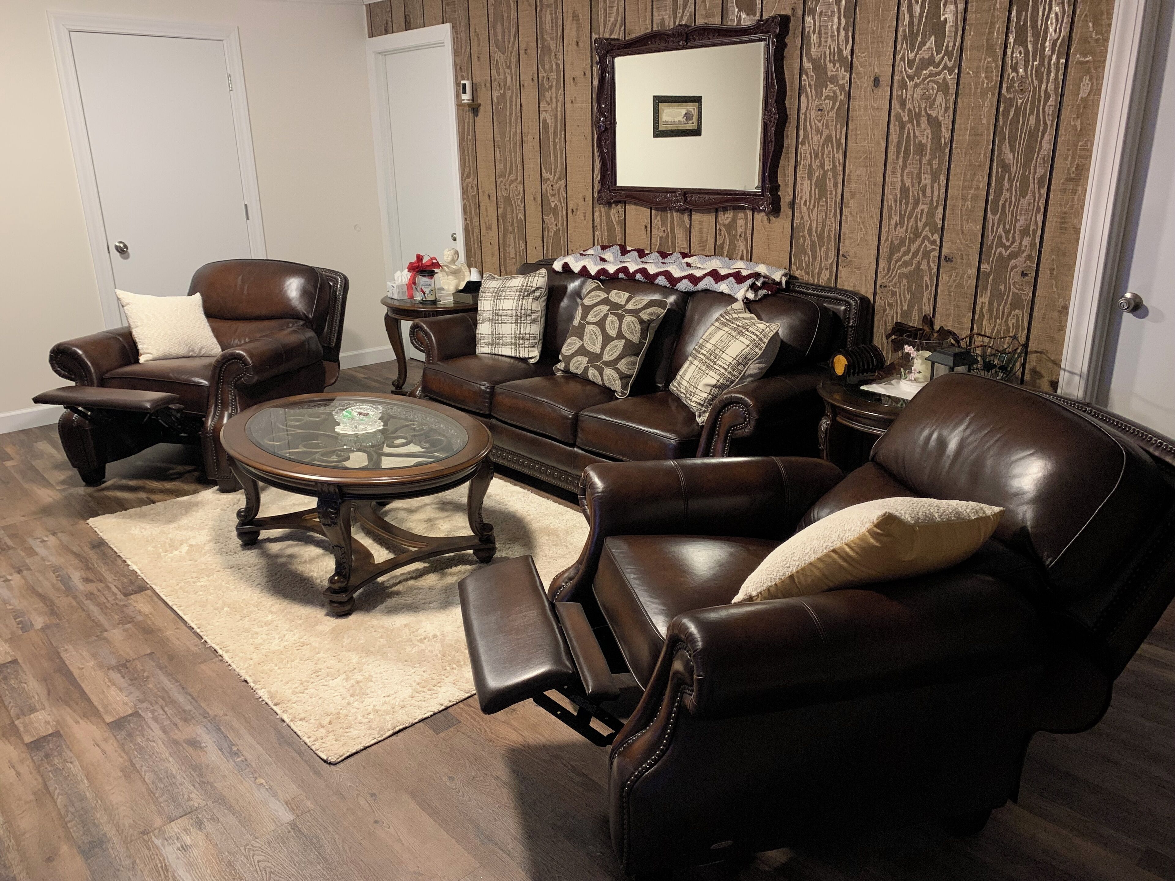 A living room with leather furniture, a glass coffee table, and a wooden wall.