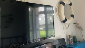A flat-screen TV mounted on a black stand, a life preserver decoration on the wall, and a small table with a radio and decorative items. - Superb studio 2 to 4 people, seaside, casino and town center (Deauville)