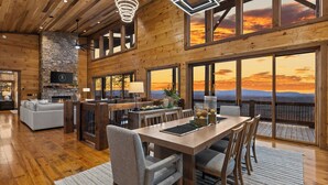 A spacious living area with a fireplace, a dining table, and a large window overlooking a scenic view. - NEW! Heated Pool + Sauna + Dog-Friendly (Mineral Bluff)