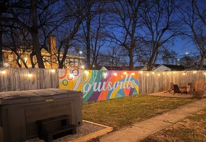 A backyard with a barbecue grill, a wooden fence, and a colorful mural with the word 'Pousville.'