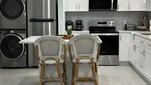 A modern kitchen with stainless steel appliances, white cabinetry, and two wicker chairs at a breakfast bar.