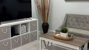 A modern living room with a flat-screen TV, a grey sofa, a coffee table with a plant, and a wall-mounted painting.