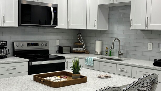 A modern kitchen with white cabinetry, a built-in microwave, a stainless steel stove, and a central island with bar stools.