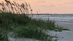A sandy beach with grass and a sign in the distance.