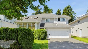 Ein zweistöckiges Haus mit Garage, umgeben von gepflegten Hecken und einem großen Felsen.