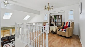 Ein geräumiger Wohnbereich mit weißer Geländer, einer Couch, einem Sessel, einer Chandelier und einem Bücherregal.