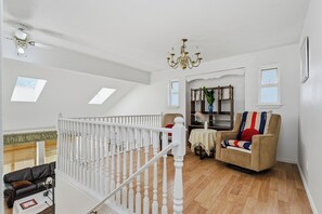 Een ruime woonkamer met een witte balustrade, een bank, een fauteuil, een kroonluchter en een boekenkast.