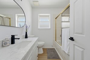 Een badkamer met een wit wastafel, toilet, douche met glazen deur en een klein raam.