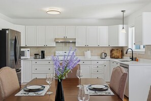Une cuisine moderne avec des armoires blanches, des appareils en acier inoxydable et un coin repas avec une table dressée pour deux personnes.