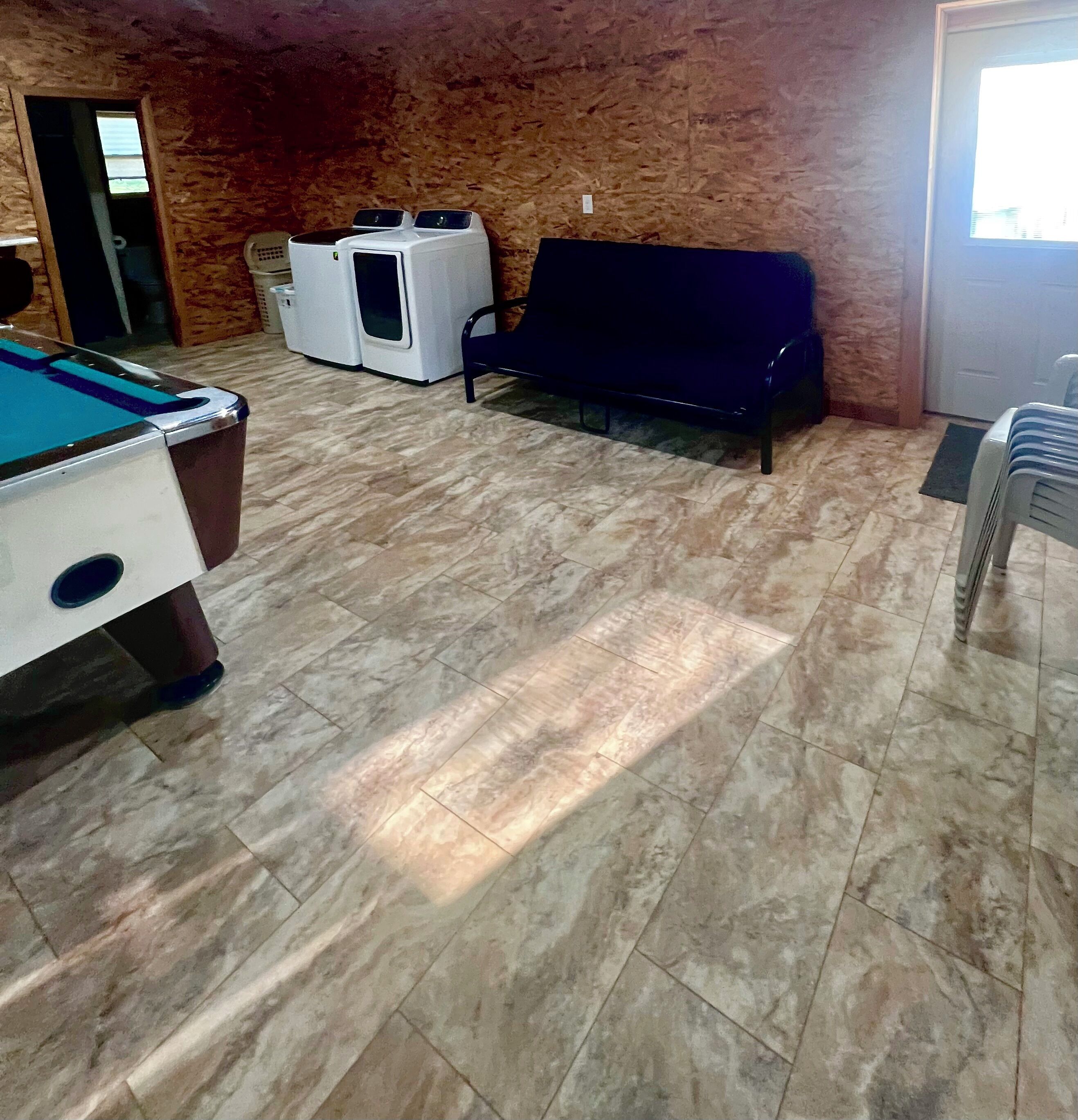 A billiards table, a sofa, and a washing machine in a room with tiled flooring and a wooden wall.