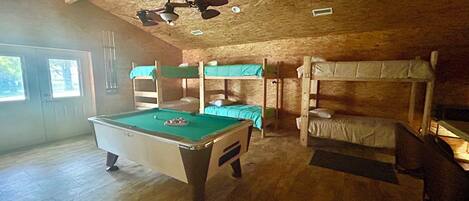 A room with bunk beds, a pool table, and a ceiling fan.