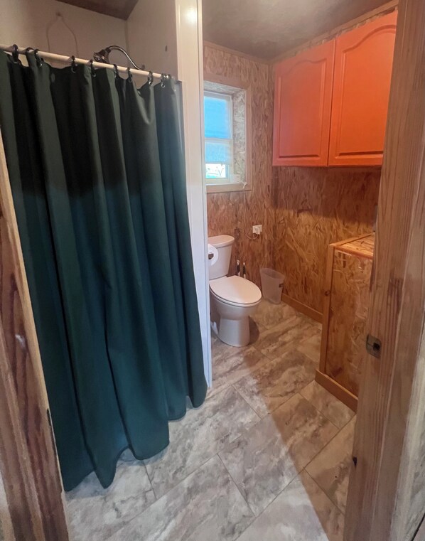 Un baño con inodoro, cortina de ducha y armarios de madera.