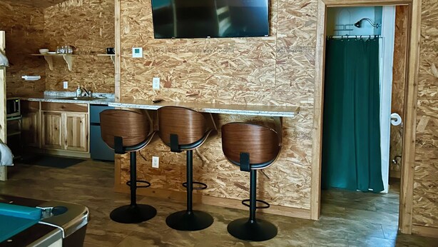 Baarialue, jossa on puuseinä, litteänäyttöinen televisio ja kolme jakkaraa.