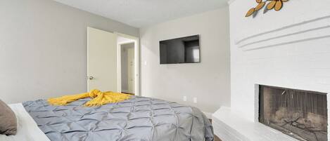 Une chambre à coucher avec un lit, une cheminée, un téléviseur et une porte donnant sur une autre pièce.