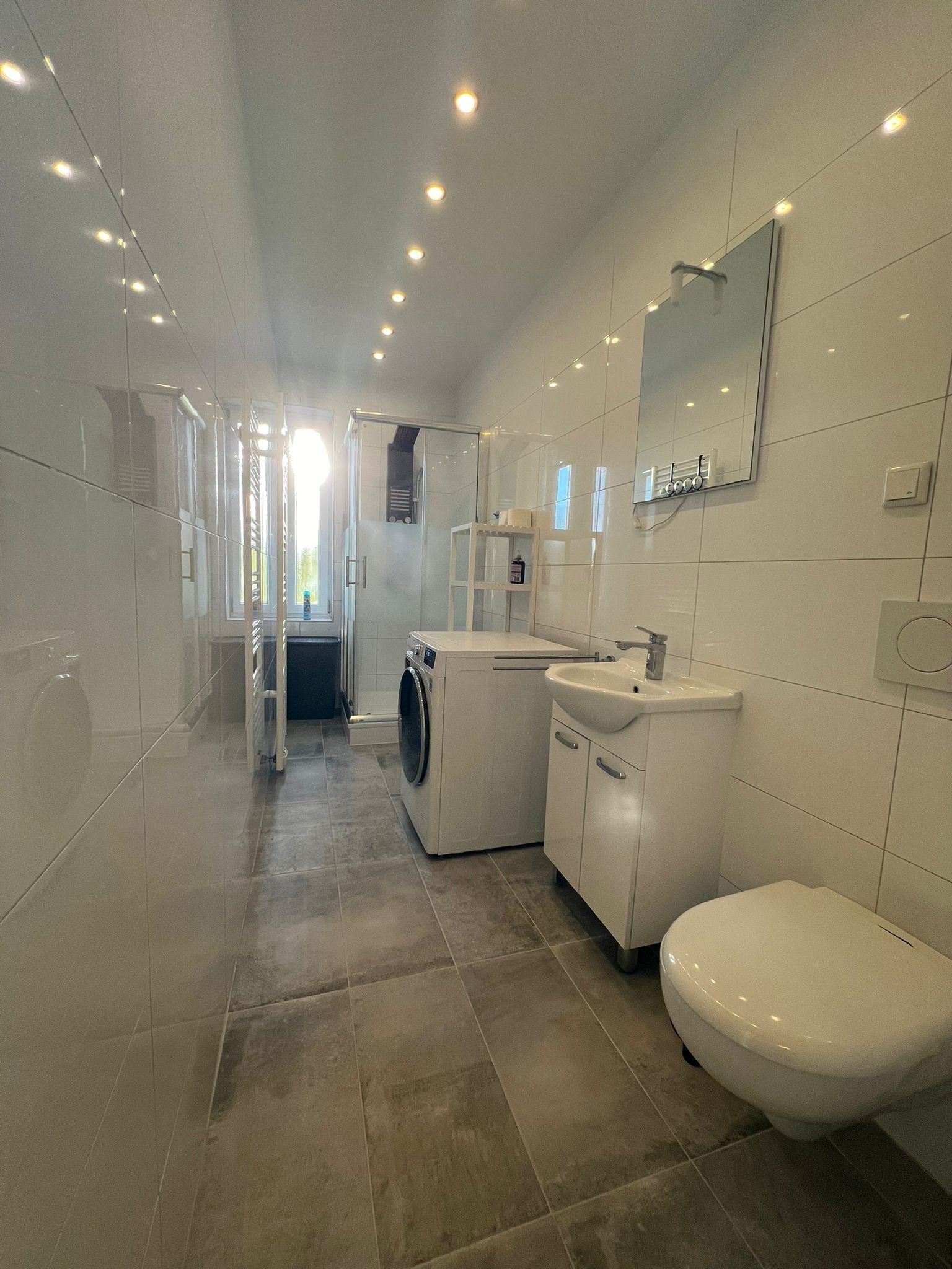 Une salle de bain moderne équipée d’une douche, de toilettes, d’un lavabo et d’un lave-linge.