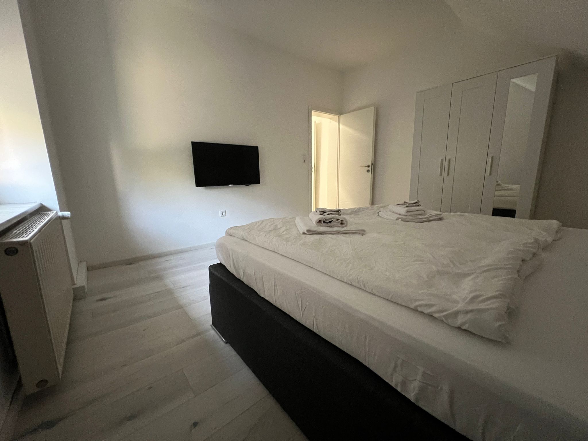 Ein Schlafzimmer mit einem Bett, einem an der Wand befestigten Flachbildfernseher, einem Kleiderschrank und einem Heizkörper.