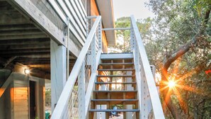 A wooden staircase leading to a covered area with a concrete floor and a metal railing. - Beachside Family Getaway Nestled in the Woods at Fort Morgan, AL (Gulf Shores)